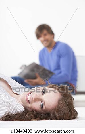 Stock Photo - Woman lying on rug, man reading. Fotosearch