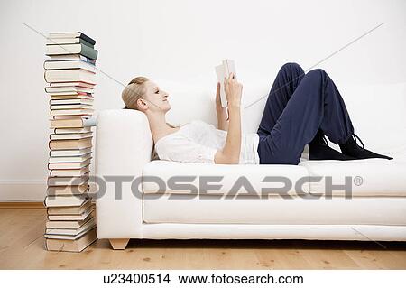 Picture - Woman reading a book on sofa. Fotosearch