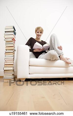 Stock Image - Woman reading a book on sofa. Fotosearch