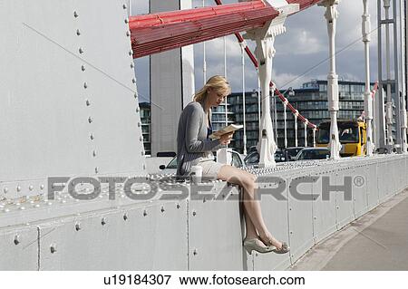 Stock Photo - Woman sitting on bridge looking at book. Fotosearch