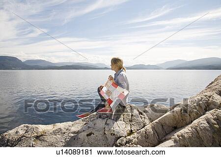 Stock Image - Woman sitting on rock by sea with kite. Fotosearch