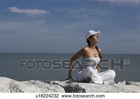 Stock Image - Woman sitting on rocks by the sea. Fotosearch
