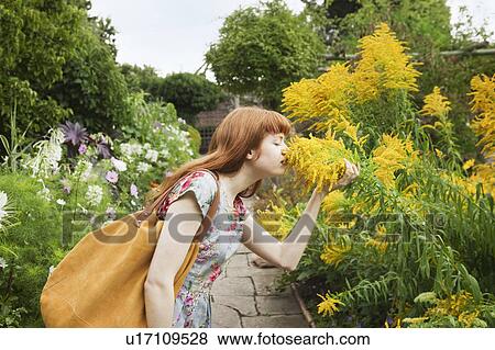 Stock Photo - Woman smelling flowers in park. Fotosearch