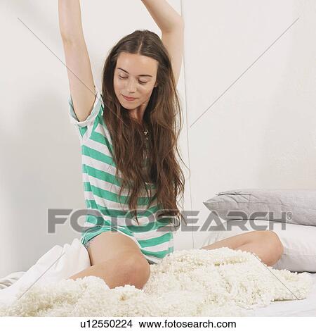 Picture - Woman stretching whilst sitting on bed. Fotosearch