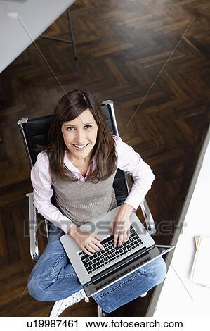 Stock Image - Woman typing on laptop looking to camera. Fotosearch