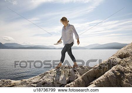 Woman walking on rocky beach by sea View Large Photo Image Stock Photo - Woman walking on rocky beach by sea. Fotosearch