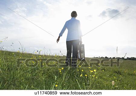 Stock Photo - Woman walking with suitcase in field. Fotosearch