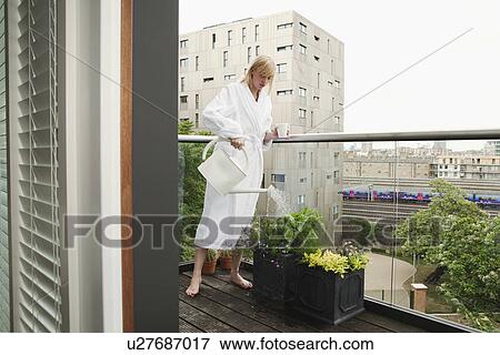 Woman watering flowers on balcony View Large Photo Image Stock Photo - Woman watering flowers on balcony. Fotosearch