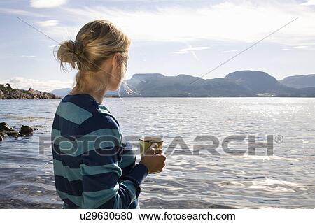 Stock Image - Woman with coffee by sea and mountains. Fotosearch