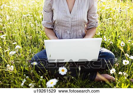Stock Photo - Woman with Laptop sitting in wild meadow. Fotosearch