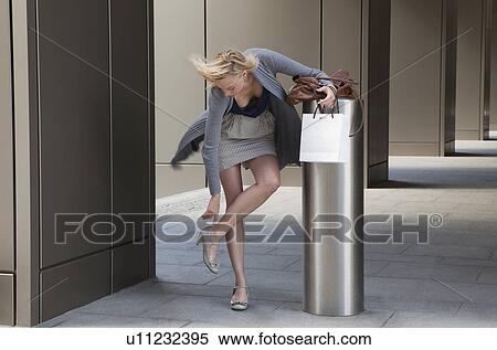 Stock Photography - Woman with shopping adjusting shoe. Fotosearch