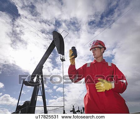 Stock Image - Worker inspecting crude oil at oil well. Fotosearch