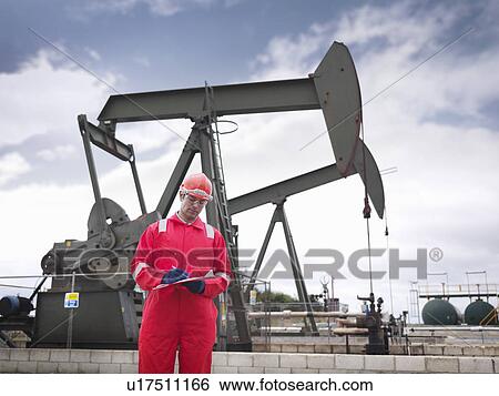Stock Photograph - Worker taking notes at oil well pump. Fotosearch