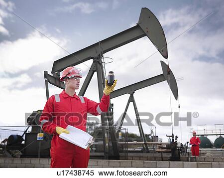 Stock Photography - Worker with oil sample and oil well pump. Fotosearch