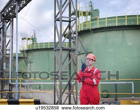 Stock Photo - Worker with radio in front of oil tanks. Fotosearch