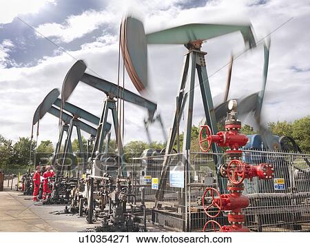 Stock Image - Workers by oil well pumps. Fotosearch
