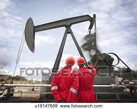 Stock Photo - Workers looking at oil well pump. Fotosearch