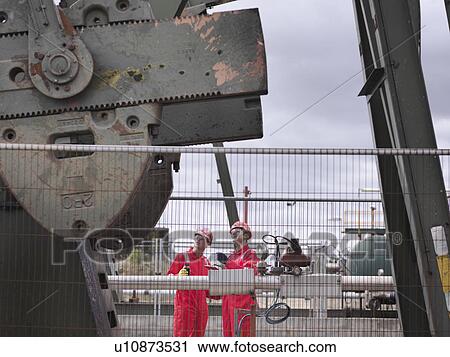 Workers looking up at oil well pump View Large Photo Image Stock Image - Workers looking up at oil well pump. Fotosearch