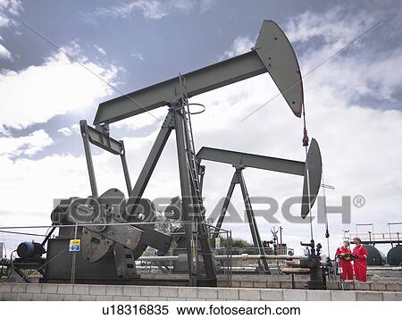 Stock Photography - Workers next to oil well pumps. Fotosearch