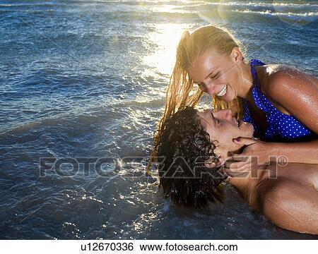 Stock Photograph - Young cple laugh lay in sea tide. Fotosearch