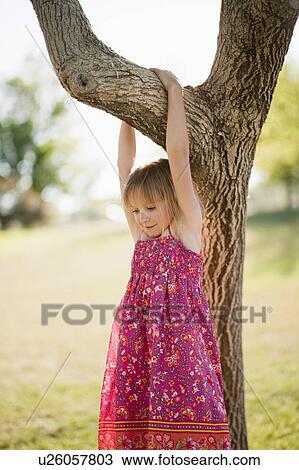 Stock Image - Young girl hanging from tree branch. Fotosearch