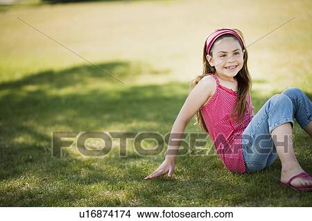 Picture - Young girl sitting on grass laughing. Fotosearch