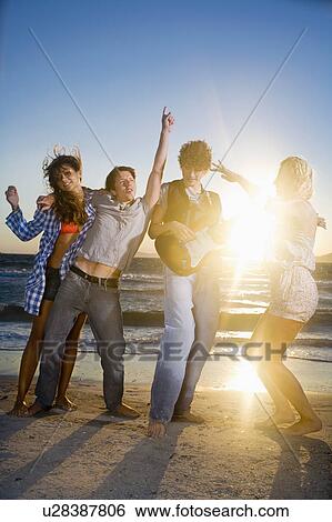 Stock Photograph - Young group with guitar dance at beach. Fotosearch