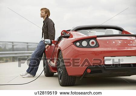 Young man filling up his electric car View Large Photo Image Stock Photo - Young man filling up his electric car. Fotosearch