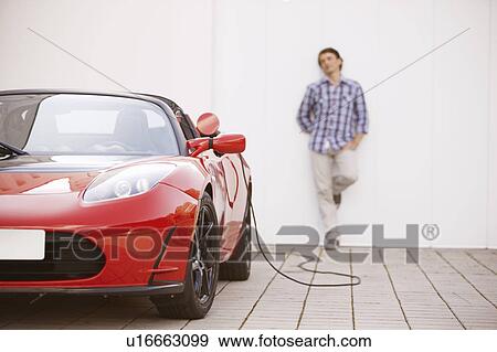 Stock Photo - Young man filling up his electric car. Fotosearch