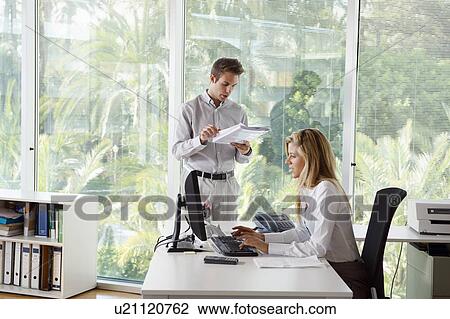 Stock Image - Young man in office with colleague. Fotosearch