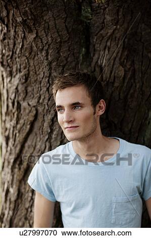 Stock Image - Young man leaning against tree. Fotosearch