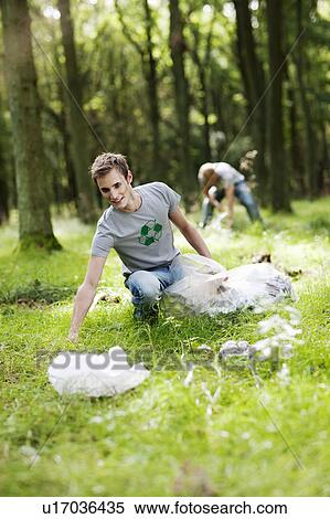 Stock Photography - Young man picking up trash in nature. Fotosearch