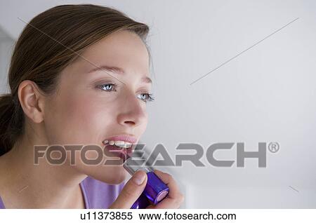 Stock Photography - Young woman applies lip stick. Fotosearch