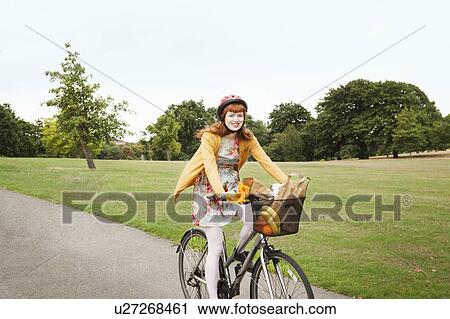 Stock Image - Young woman cycling through park. Fotosearch