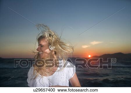 Young woman wears ear phones at sunset View Large Photo Image Stock Image - Young woman wears ear phones at sunset. Fotosearch
