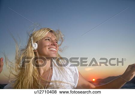 Stock Photo - Young woman wears earphones at sunset. Fotosearch
