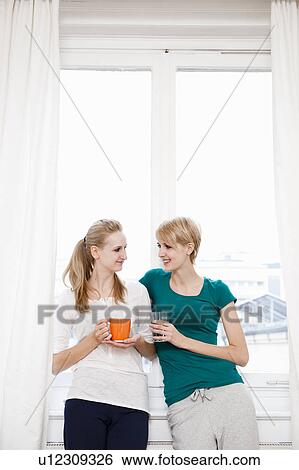 Stock Photograph - Young women chatting, drinking. Fotosearch