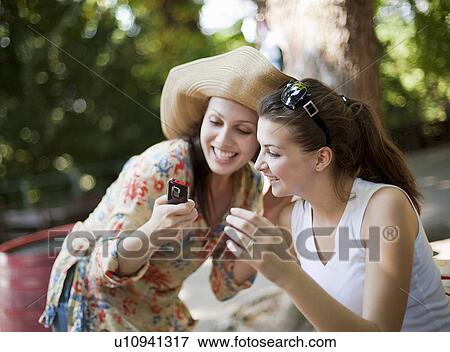Stock Photo - Young women looking at mobile phone. Fotosearch