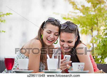 Stock Photo - Young women looking at phone in cafÈ. Fotosearch