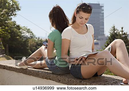 Stock Photo - Young women sitting on wall. Fotosearch