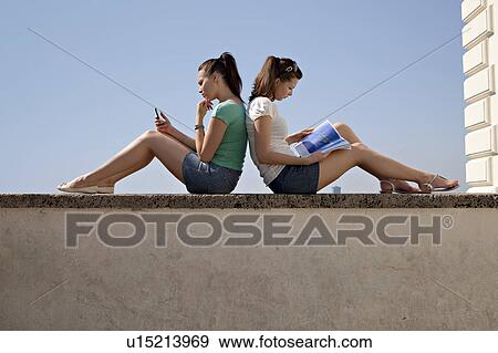 Stock Photo - Young women sitting on wall. Fotosearch