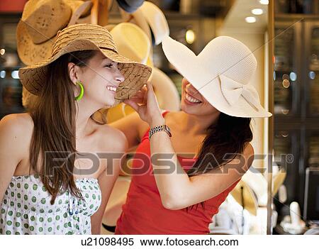 Stock Photography - Young women trying on hats. Fotosearch