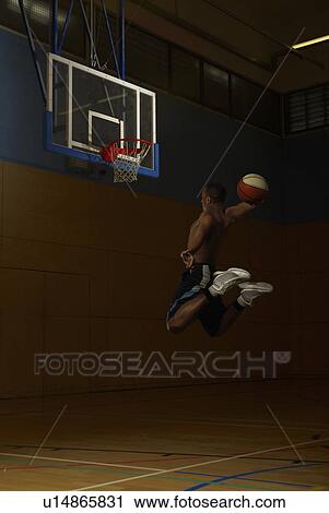 Stock Image - Basketball player jumping at goal hoop. Fotosearch