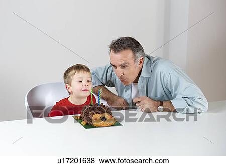 Stock Photo - Boy with dad blowing out candles on cake. Fotosearch