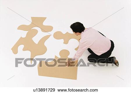 Stock Photo - Business man looks to finish puzzle. Fotosearch