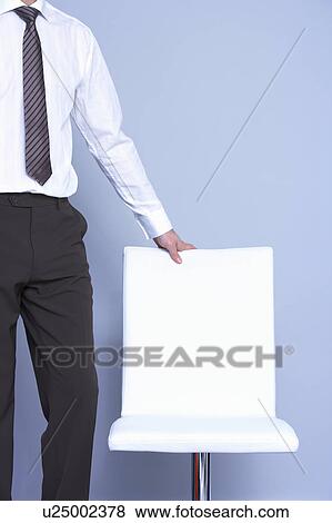 Stock Photo - business man standing next to his chair. Fotosearch