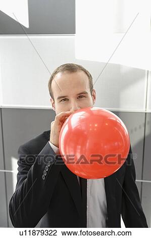 Stock Image - Businessman blowing up red balloon. Fotosearch