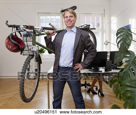 Stock Image - Businessman in office with bicycle. Fotosearch