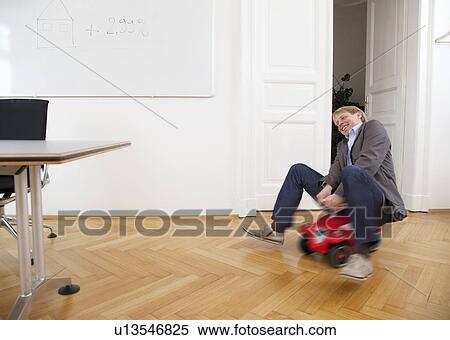 Businessman riding toy car in office View Large Photo Image Stock Photography - Businessman riding toy car in office. Fotosearch