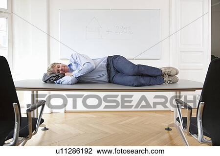 Stock Image - Businessman sleeping on conference table. Fotosearch